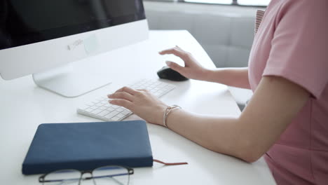 asian woman looks tired while working in front of a computer by massaging her hands in a workspace inside the office.