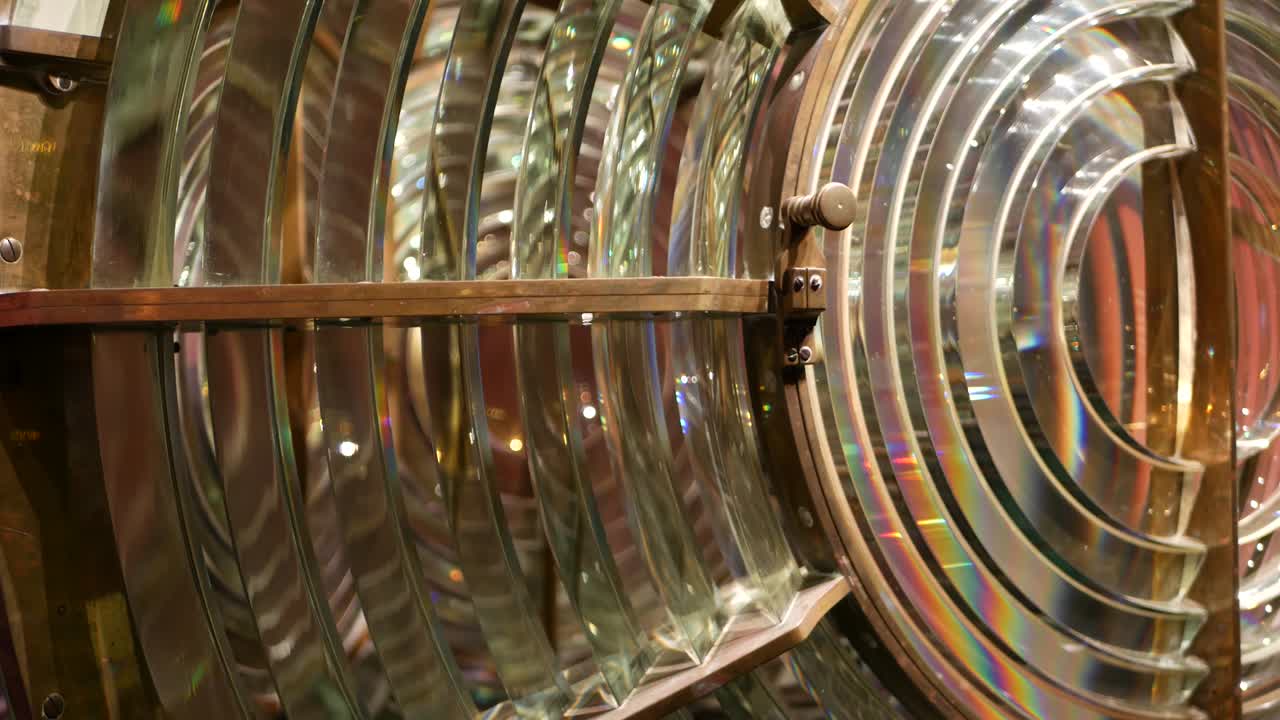 Fresnel lens with brass structure, nautical lighthouse tower. Detail of the glass lantern with rainbow spectrum. System of lamps and lenses to serve as a navigational aid. Old sea searchlight beacon.