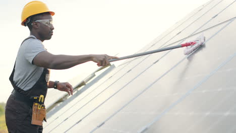 uomo afroamericano in uniforme speciale e casco protettivo che pulisce un pannello solare