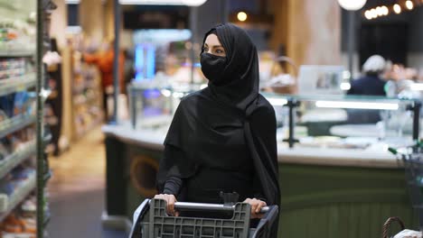 Woman-in-hijab-and-protective-mask-doing-grocery,-pushing-shopping-cart