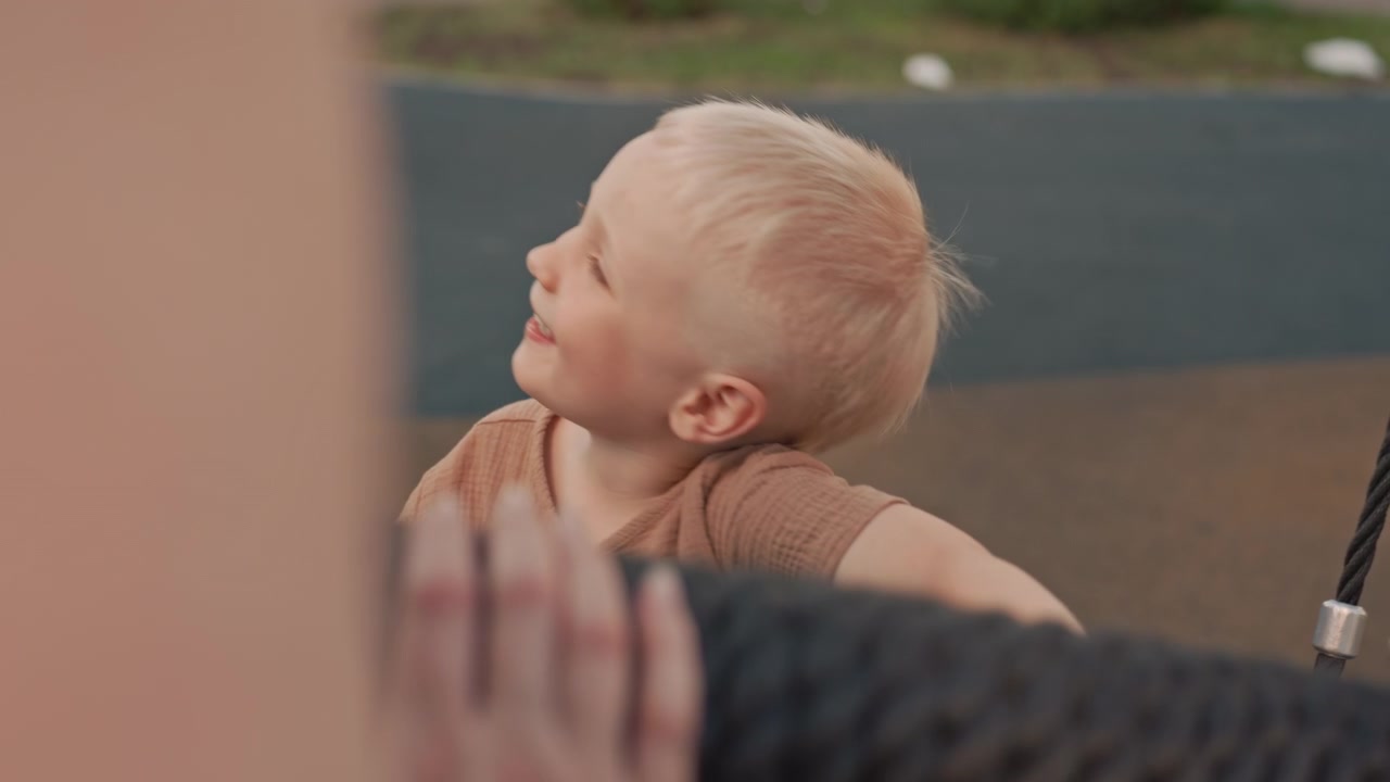 Young child enjoys swinging on tire swing at playground wearing casual clothing and surrounded by outdoor play equipment. scene captures moments of movement as boy interacts with netted rope