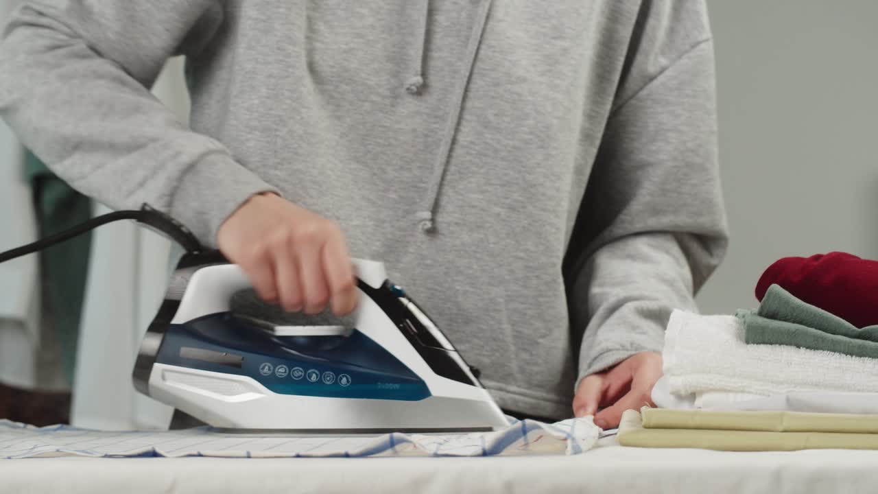 Person Ironing Clothes with a Steam Iron on an Ironing Board