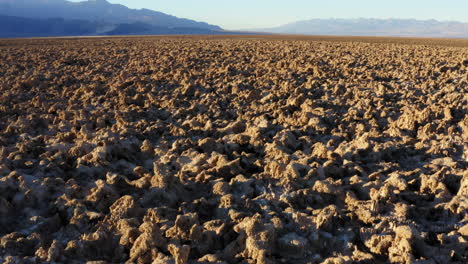 drone flying low over rugged and harsh terrain of devils golf course formed by large salt pan on floor of death valley national park