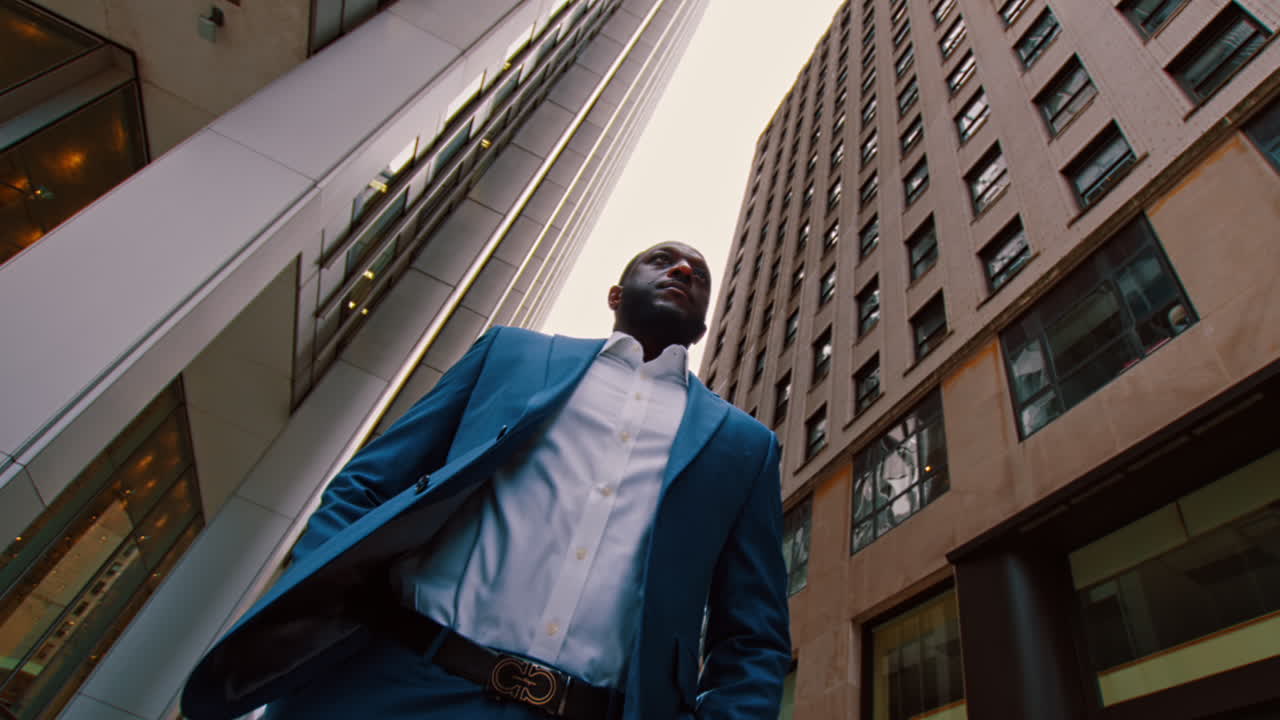 Nova York, EUA, 28 de maio de 2025: Retrato de empresário em meio aos arranha-céus da cidade de Nova York. Plano médio em ângulo baixo de um homem de terno azul em pé na rua de Manhattan, rodeado por edifícios altos.