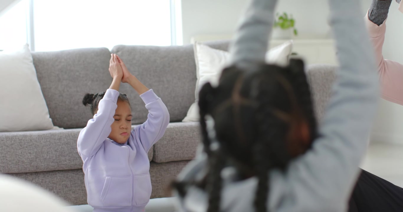 African American family mirroring senior male guiding calming stretch and breath near grey sofa