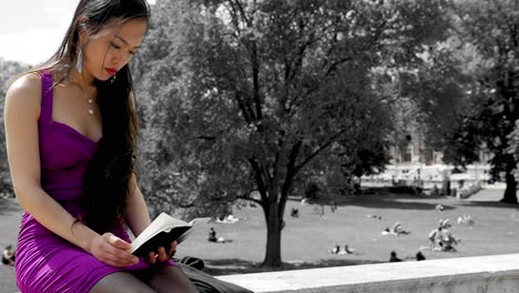 Mujer-Con-Un-Vibrante-Vestido-Morado-Leyendo-Un-Libro-En-El-Parque-Burggarten,-Viena,-Con-Gente-Descansando-En-El-Fondo,-Un-Día-Soleado