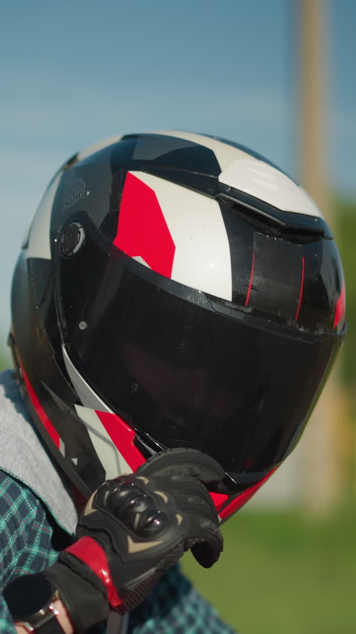 una motociclista femenina con casco y guantes de protección negros baja su visera, preparándose para montar, lleva equipo completo, con un fondo borroso