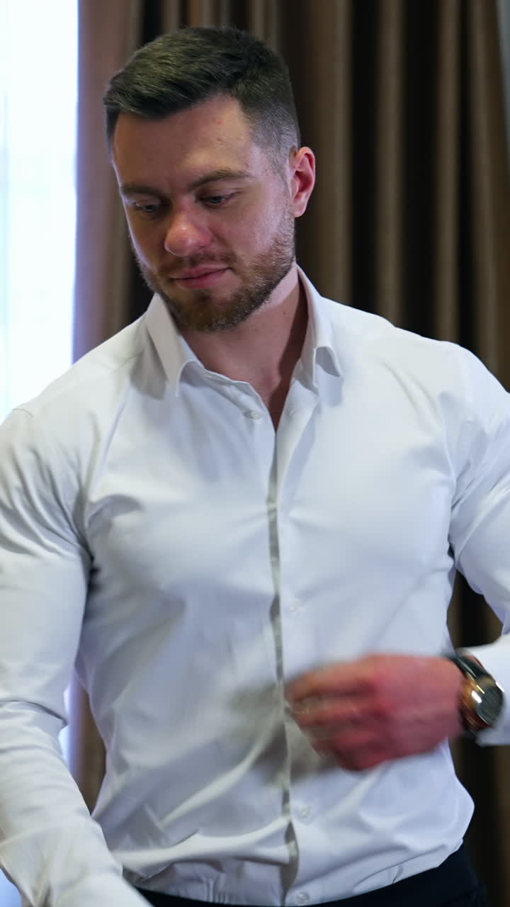 Successful businessman near the window. Handsome man in white shirt at modern room in a hotel. Bearded young man on the background of luxury curtains. Vertical video