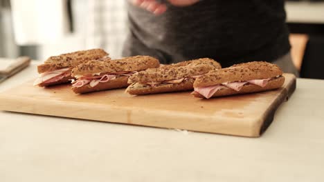 Caucasian-male-displaying-home-male-deli-baguettes-on-wooden-chopping-block-in-the-kitchen