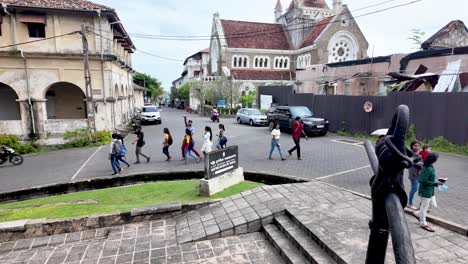 view of all saints' church in galle, nestled among historic buildings with visitors walking and cars passing by, capturing the essence of cultural architecture and local life.