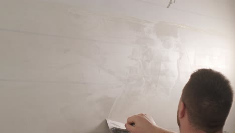 man plastering the walls with finishing putty in room with putty spatula