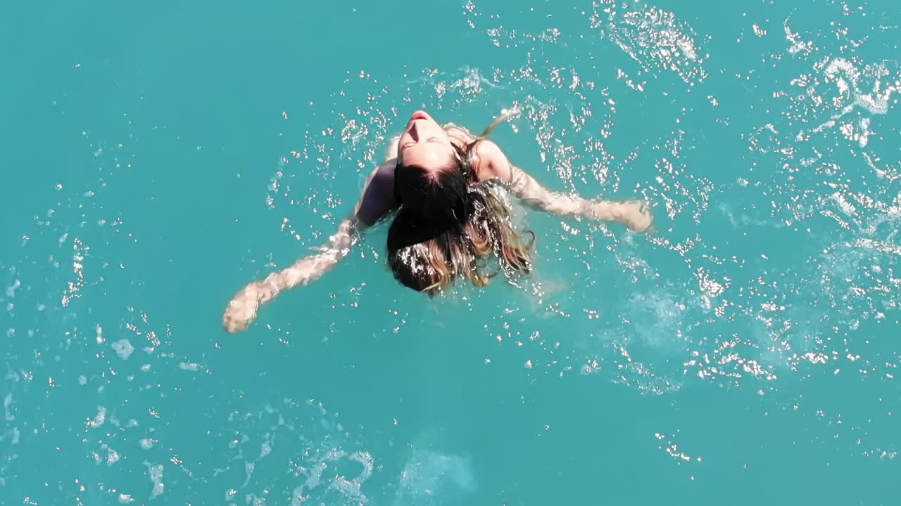 Donna caucasica in costume da bagno bianco che saltella in acqua verde e trasparente. Vista dall'alto. Slow motion