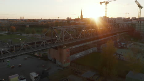 Establecimiento-De-Una-Toma-Del-Icónico-Tren-Subterráneo-Amarillo-De-Berlín-Que-Pasa-Por-Un-Puente-En-Un-Hermoso-Vecindario-Con-Puesta-De-Sol,-Toma-Aérea-De-Drones