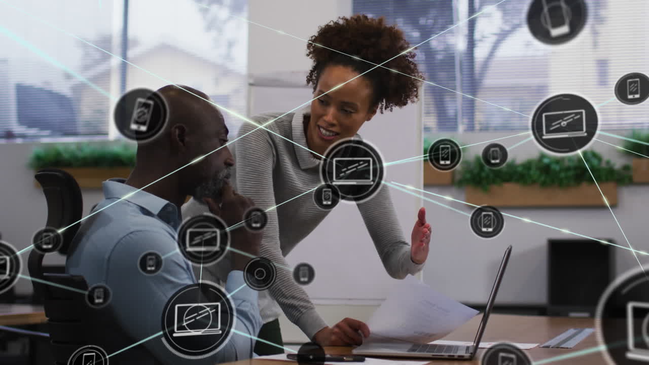 Animation of connected icons over diverse coworkers discussing reports on laptop in office