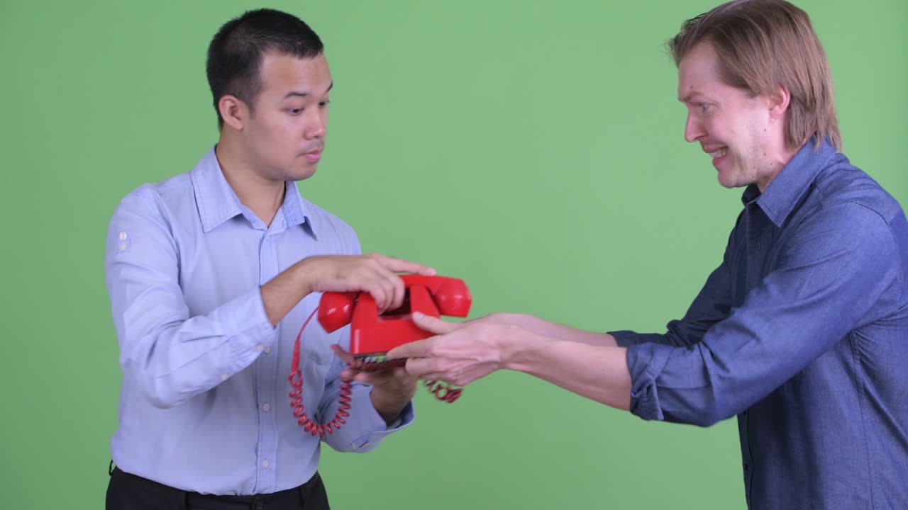 el hombre de negocios caucásico trae el teléfono al hombre de negocios asiático mientras da malas noticias contra el fondo del estudio verde