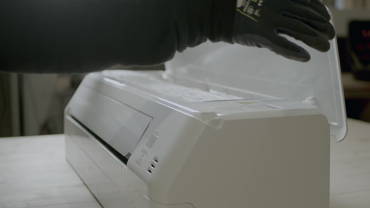 장갑을 끼고 있는 전기 기술자가 유지 보수를 위해 에어컨 덮개를 엽니다.