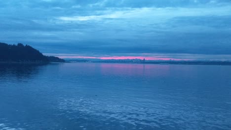 On-the-bow-of-the-Bremerton-Seattle-Ferry-during-the-blue-sunrise-hour,-calm-water,-golden-glow-in-the-clouds