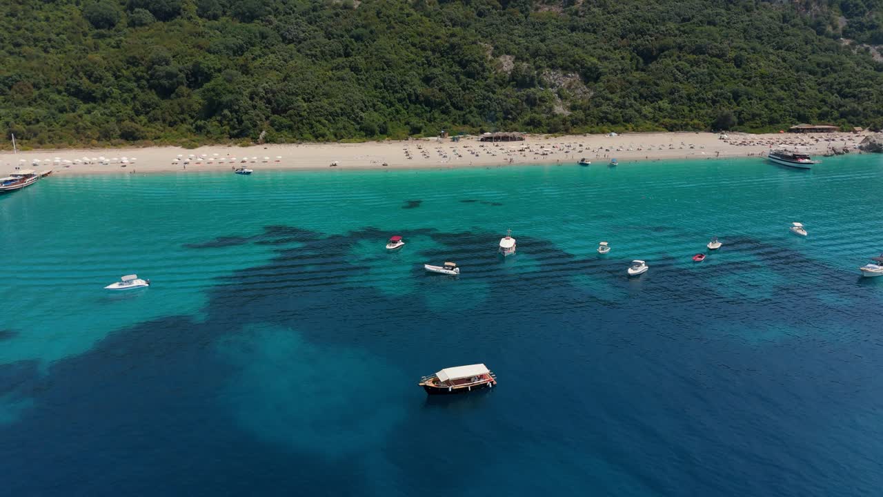 Boats float on crystal clear waters near a secluded beach with green hills in Albania