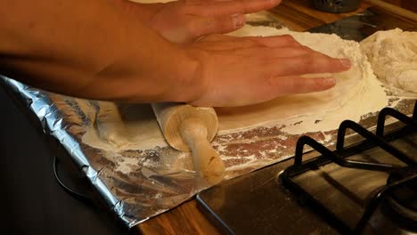 Amateur-pizza-maker-stretching-the-pizza-dough-using-wooden-rolling-pin-in-domestic-kitchen