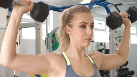 young woman shoulder pressing dumbbells at a gym