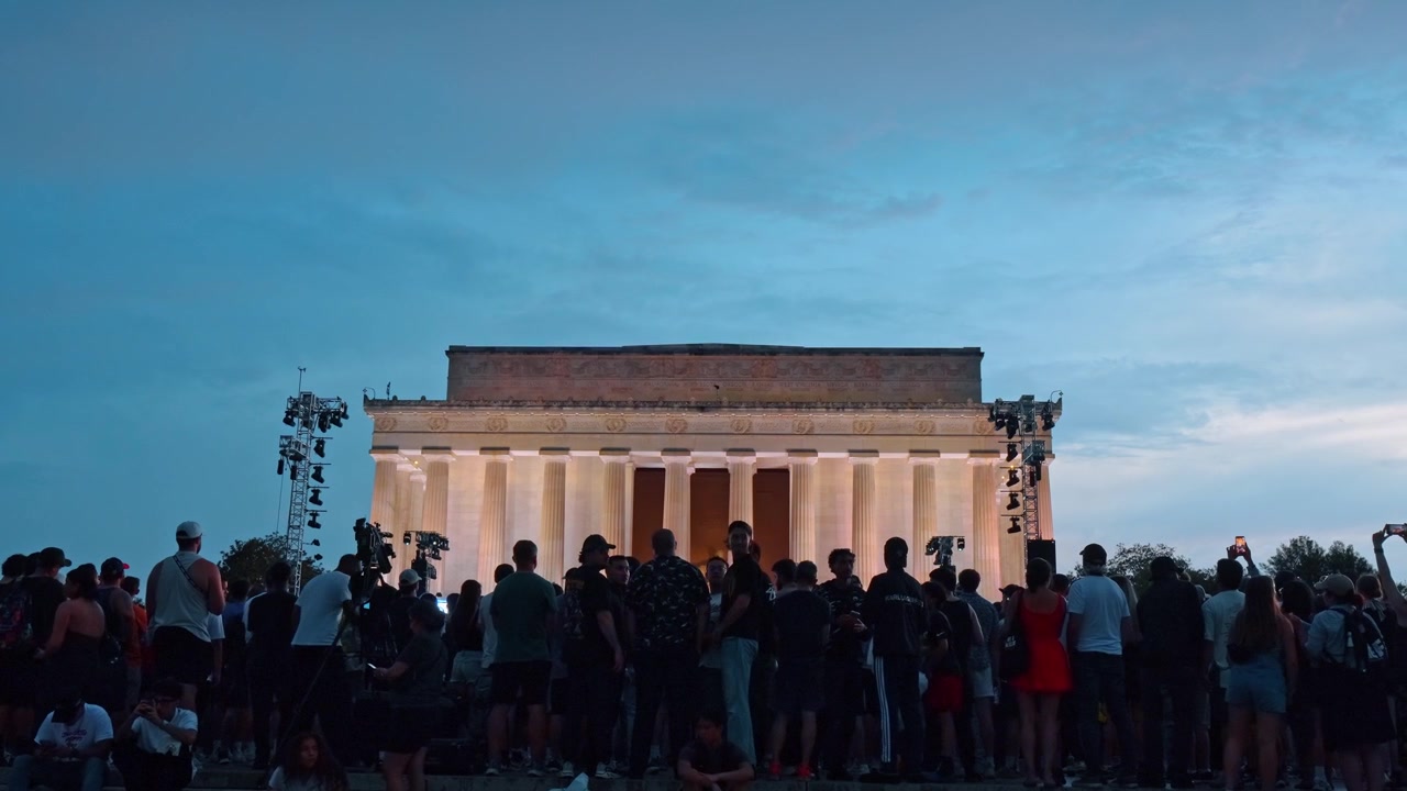 Washington, USA, 13 June 2026: Dusk gathering at Lincoln Memorial with warm facade lighting. Frontal view of crowds, light towers and soft blue evening sky above columns.