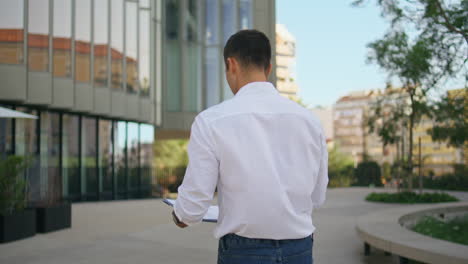 elegant businessman holding folder studying documents at street on go back view