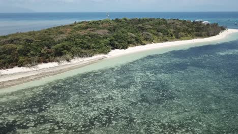 antena de drones que desciende hacia una playa de arena blanca en una isla tropical junto a un arrecife azul claro