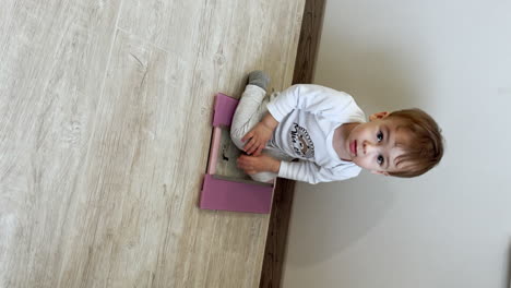 cute baby boy sits on the floor near the scales. kid climbs on the weights and looks up at camera. top view. vertical screen.