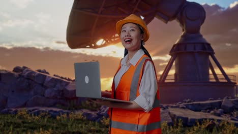side view of asian female engineer with safety helmet working on a laptop and looking around while standing with large satellite dish