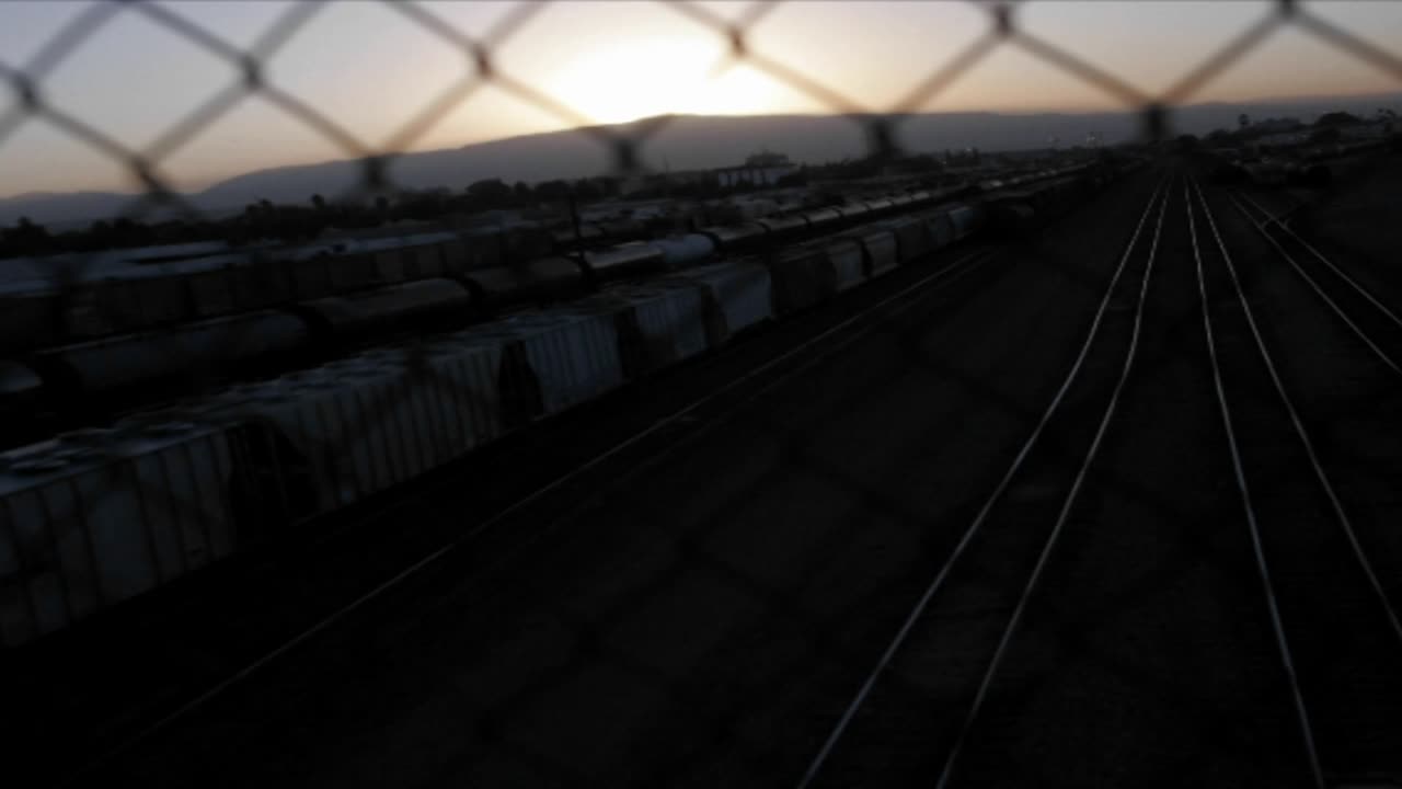 A time lapse shot through a chain link fence of a railway freight yard