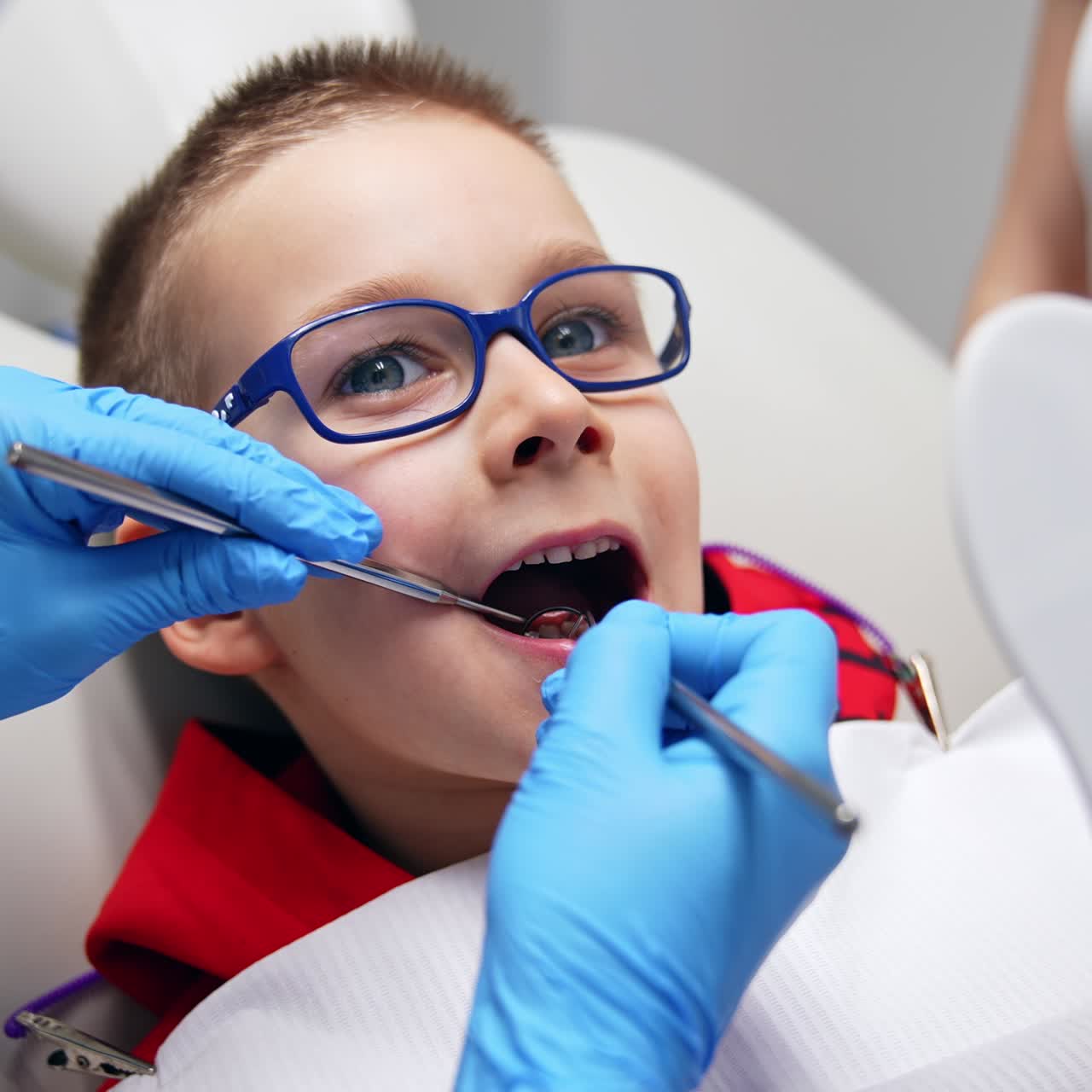 A boy opened mouth wide and doctor holding metal tools in his mouth showing the result of work. Little patient looking at his teeth in a mirror. Close up