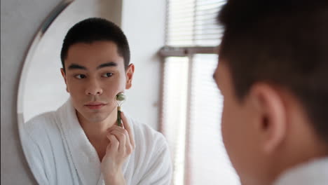 man using jade roller in front of mirror