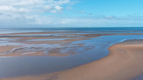 Luftaufnahme,-Spur-Vorwärts,-Die-Ebbe-An-Einem-Strand-Mit-Gezeitentümpeln,-Die-über-Den-Sand-Wirbeln,-Während-Sich-Der-Blaue-Himmel-Im-Wasser-Spiegelt,-Waldstrand,-Hoher-Norden-Von-Queensland,-Australien