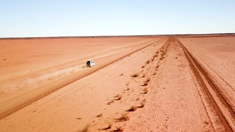 Drone-Siguiendo-El-Coche-Con-Un-Gran-Rastro-De-Polvo-Mientras-Viaja-Por-Un-Camino-De-Tierra-Desolado,-Abierto-Y-Plano