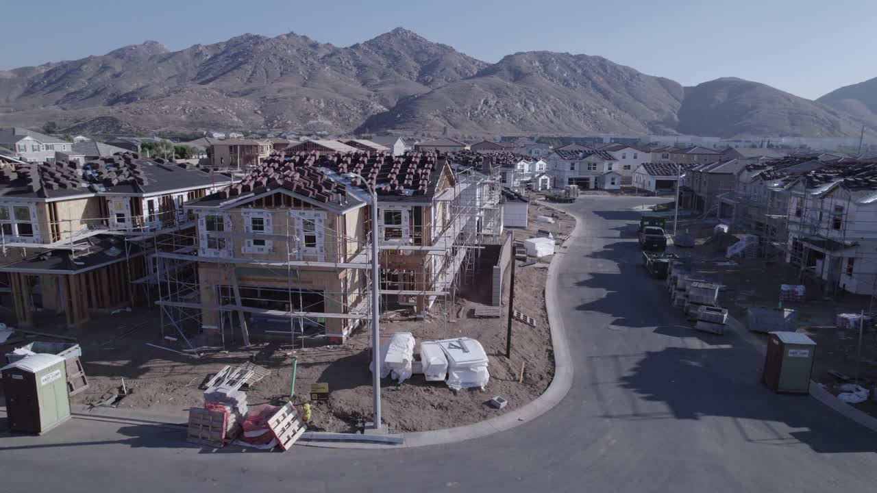 With a deliberate pace, a drone closely inspects a partially built house on a construction site from a medium distance, providing a detailed view of the ongoing progress in residential development