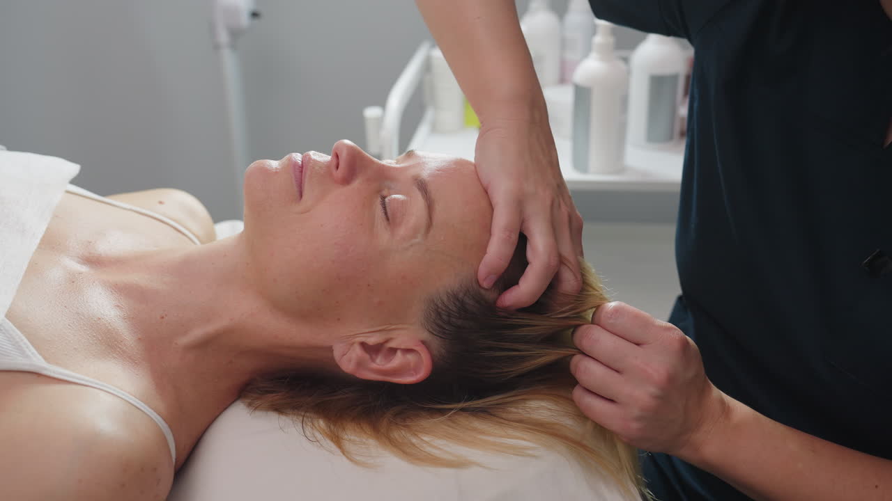 Skin care expert gently massages head and neck of relaxed client lying on spa table with soothing finger glides through hairline and neck muscles to release tension and encourage calm in serene spa