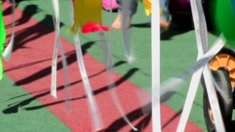 Ribbons-of-various-colors-hanging-that-move-with-the-wind-projecting-a-shadow-on-the-ground,-children's-feet-running-between-them,-very-beautiful