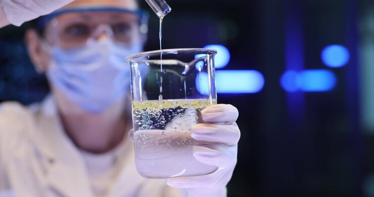 Woman scientist pours clear liquid from tube into lab beaker