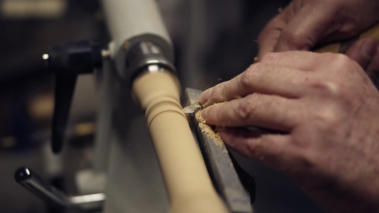 Carpenter male hands cutting wooden knob out of wood piece spinning on machine using chisel, close up shot. Slow motion