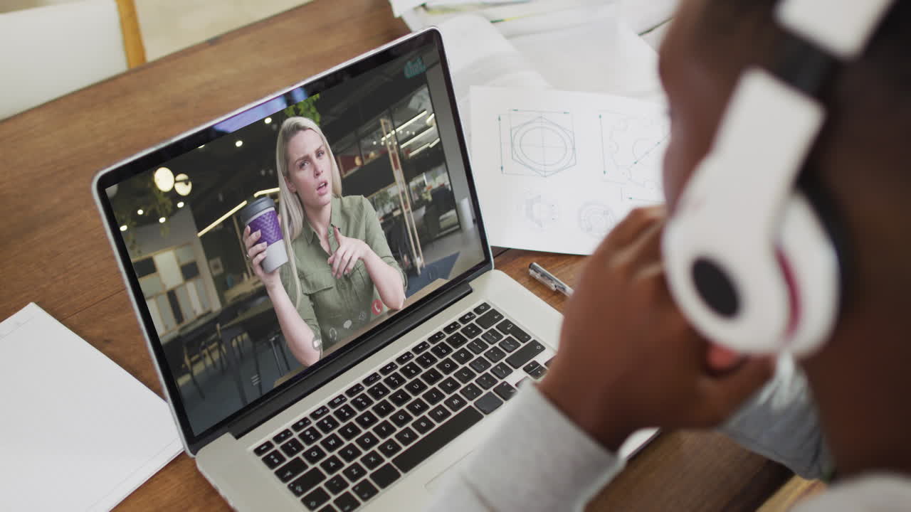 African american male college student holding notes while having a video call on laptop at home