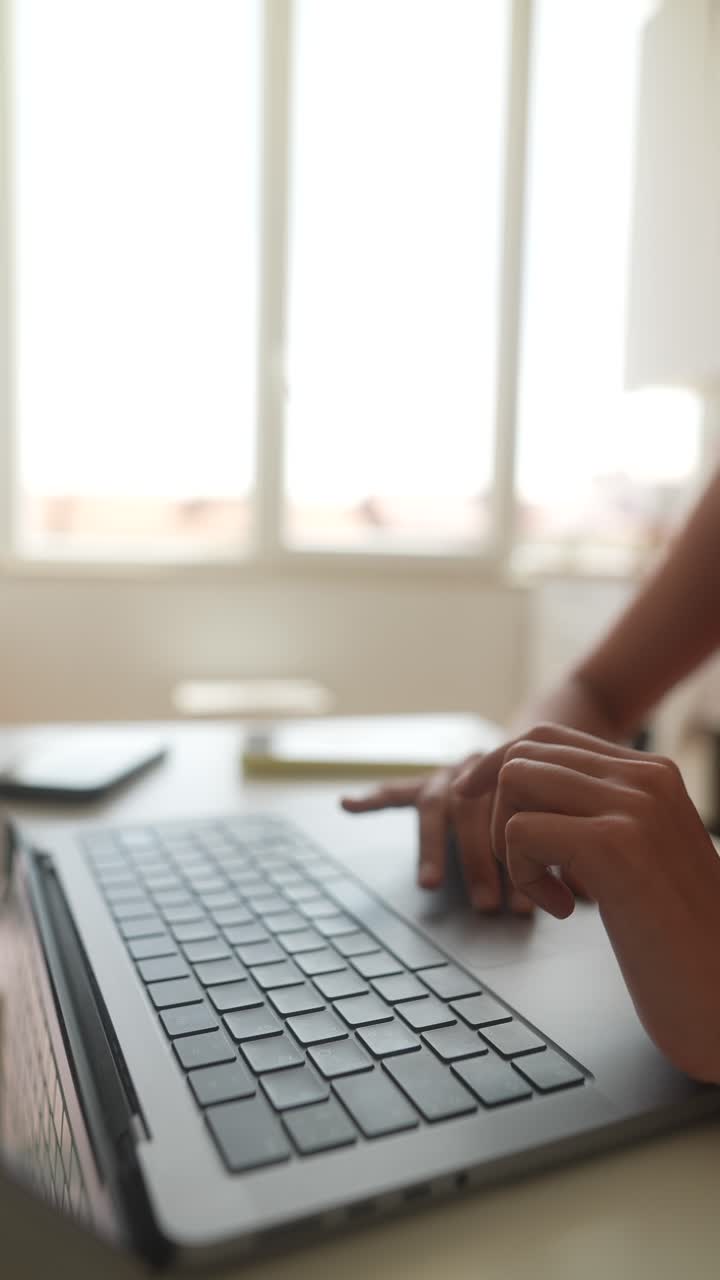 Primo piano di mani che digitano sulla tastiera del portatile accanto a una finestra