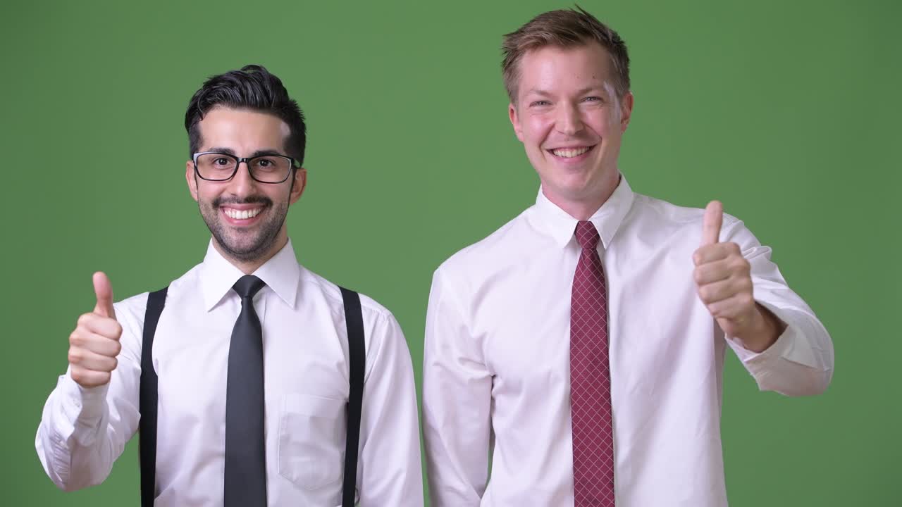 Two young multi-ethnic businessmen working together against green background