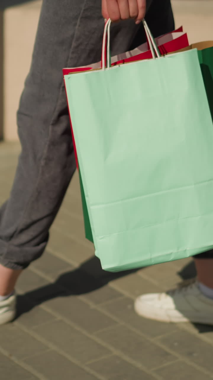 vista de la pierna de un individuo caminando por un camino entrelazado cerca de una valla mientras lleva una bolsa de compras, mientras el sol proyecta su sombra mientras camina
