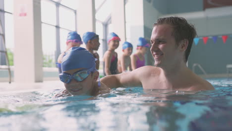 male swimming coach giving boy holding float lesson in pool