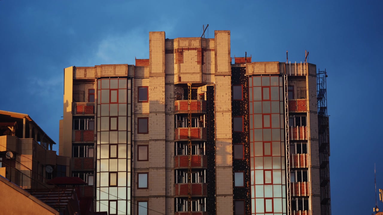 Edificio residenziale di media altezza in costruzione con sezioni in mattoni a vista, facciata in cemento non finita, pannelli di vetro installati e impalcature visibili sul lato destro.