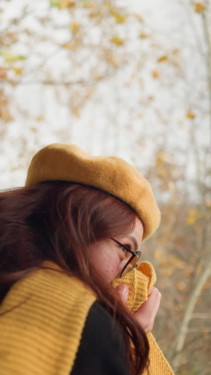 선글라스를 입은 은 물결 모양의 머리카락을 가진 여자의 가까운 머리 모습, 흥분하고 자연을 즐기고, 그녀의 입을 기 위해 그녀의 무플러를 사용하여 약간 구부립니다.