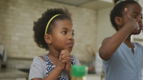 Happy-african-american-girls-eating-and-waving-hands-in-kitchen