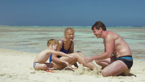 parents and son playing with sand on the beach