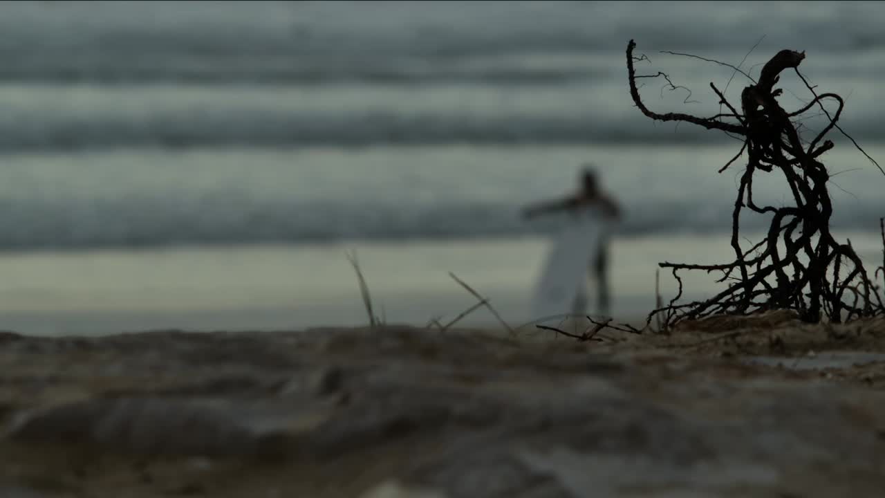 Verschwommener Surfer am Strand mit einigen Stöcken im Vordergrund