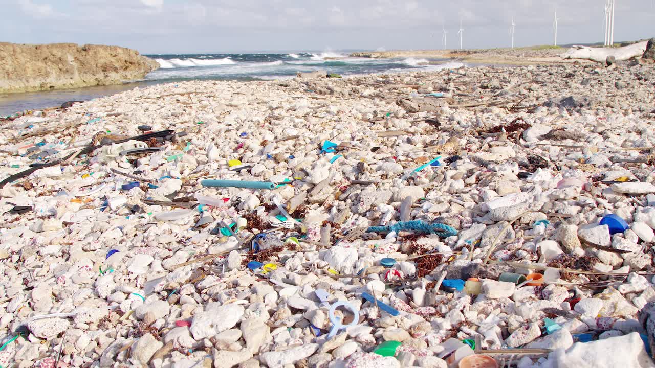 사람이 만든 플라스틱 파편과 쓰레기의 기울기가 카리브해의 바위 해안에서 천천히 씻겨지고 있다